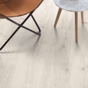 White Bayfoard Oak Aqua laminate flooring shown in a bright room setting with chair and side table.