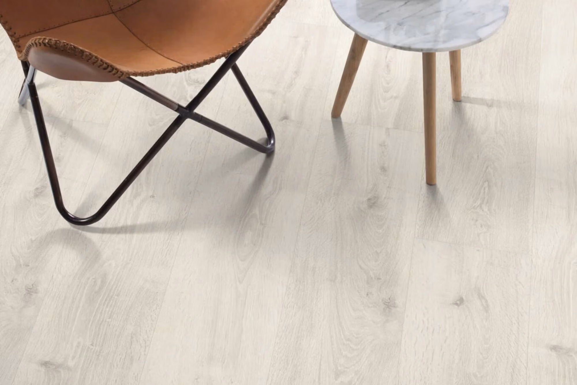 White Bayfoard Oak Aqua laminate flooring shown in a bright room setting with chair and side table.